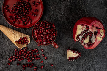 on a black, stone background, bloody red pomegranate seeds in a red cup and on a red plate