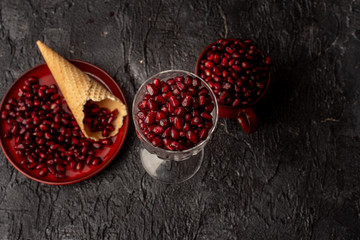 on a black, stone background, bloody red pomegranate seeds in a red cup and on a red plate