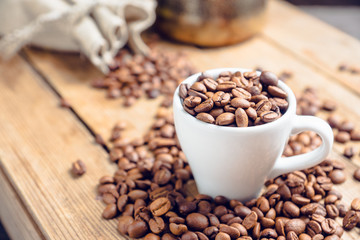 Coffee beans in white cup on the rustic wooden background. Selective focus. Shallow depth of field.