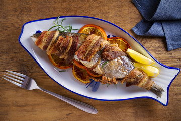 Grilled bacon-wrapped fish with oranges and rosemary, served with lemons - Image