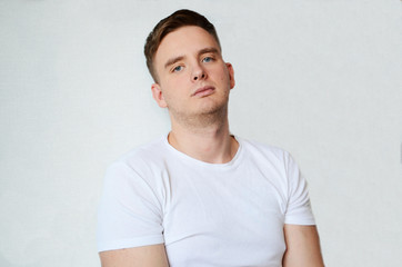 young man with blond hair on a white background in a white T-shirt looks tired and does not smile, isolated