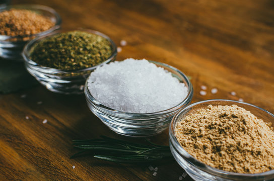 Round glass spice bowl on a wooden table - ground ginger, hops-suneli and sea salt.