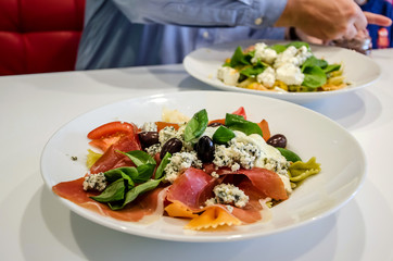 Delicious Italian pasta in a plate on a white table in a restaurant. Man in the background.