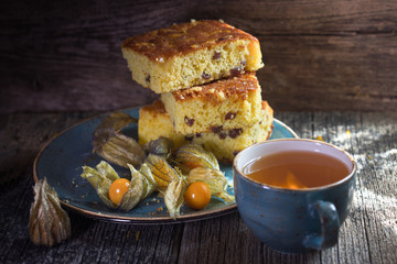 Three pieces of delicious biscuit lie on a plate next to the orange berries of physalis. And a Cup of hot tea is on the gray boards of the kitchen table.