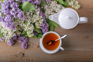 Bouquet of lilac, a cup of tea, a white teapot on a wooden table.