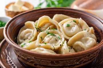 Traditional russian homemade meat dumplings pelmeni with butter and greens in ceramic bowl on white wooden table. Selective focus.