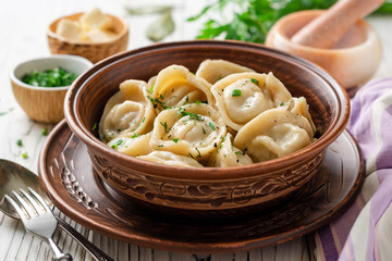 Traditional russian homemade meat dumplings pelmeni with butter and greens in ceramic bowl on white wooden table. Selective focus.