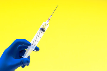 Hand in a blue glove holding syringe on yellow background