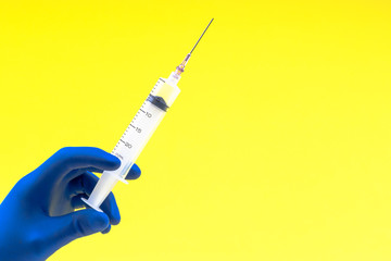 Hand in a blue glove holding syringe on yellow background