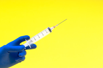 Hand in a blue glove holding syringe on yellow background