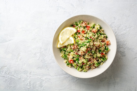 Traditional Arabic Salad Tabbouleh with couscous, vegetables and greens on concrete background. Top view. Copy space.
