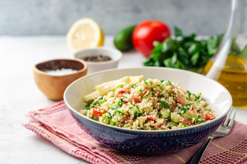 Traditional Arabic Salad Tabbouleh with couscous, vegetables and greens on concrete background. Selective focus.