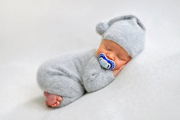 Sleeping newborn boy with baby's dummy in the first days of life on white background