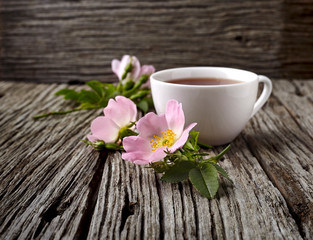 Rosehip flowers and cup of healthy tea, herbal medicine. A cup of  tea with rosehip on the wooden background