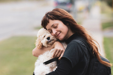 Young woman hugging a white adorable Maltese and Poodle mix Puppy (or Maltipoo dog)