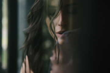 Young sexy brunette woman in suit smoking a cigarette by the window indoors