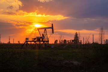 The equipment for oil and gas production works at sunset in the rays and glare of the sun. Oil well at sunset. Oil production with rocker at sunset. Rocking oil