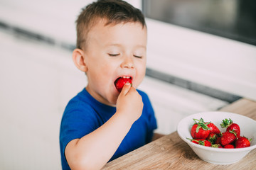 Baby boy in the kitchen eating strawberries very ripe and tasty, stocked with vitamins