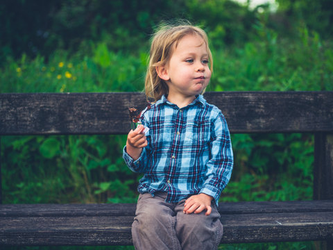 Little toddler eating a fruit bar on a bench