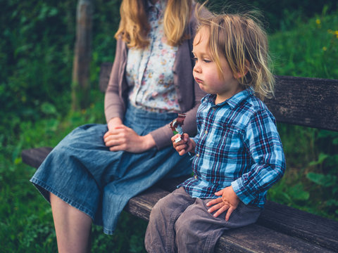 Little toddler eating fruit bar with his mother on bench