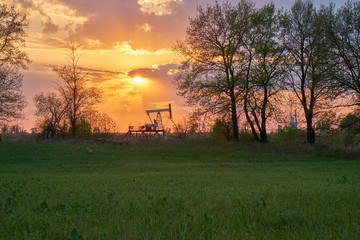 The equipment for oil and gas production works at sunset in the rays and glare of the sun. Oil well at sunset. Oil production with rocker at sunset. Rocking oil