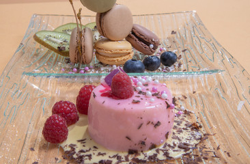 Raspberry mousse on a glass plate and colorful butter cream macarons