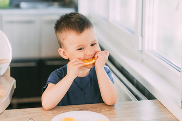 Beautiful Baby boy in the kitchen eagerly eating an orange, cut into wedges