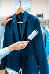 Woman in dry cleaning store is using lint roller to clean a jacket