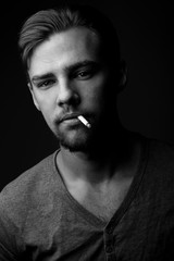 Portrait of a young Caucasian Smoking man with a cigarette in his mouth and short beard and mustache on a dark background, black and white