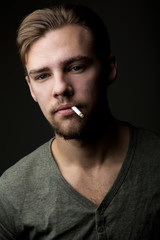 Portrait of a young Caucasian Smoking man with a cigarette in his mouth and short beard and...