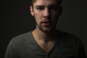 Obraz premium Portrait of a young Caucasian Smoking man with a short beard and mustache on a dark background