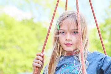Portrait of little cute blond girl with blue eyes swinging. Close up portrait
