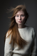 beautiful redhead model girl with long hair in the Studio on a gray background in a jacket of large knit