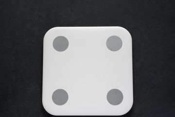 White modern scales on dark gray black background with copy space for weight control and fitness. Flat lay
