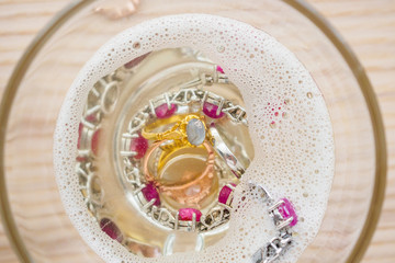 cleaning vintage jewelry diamond ring and bracelet in glass on wood table background