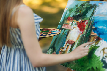 Back view of beautiful blond hair girl drawing a picture in the park. mid celection