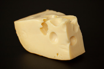 Big chunk of Swiss Emmental cheese isolated on black.