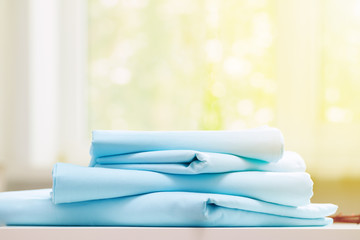 Closeup stack of blue clean bedding on blurred background. Sunlight from the window.