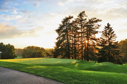 Beautiful summer evening nature background. Scenic view with setting sun after rainy day and cloudy sky over golf course.