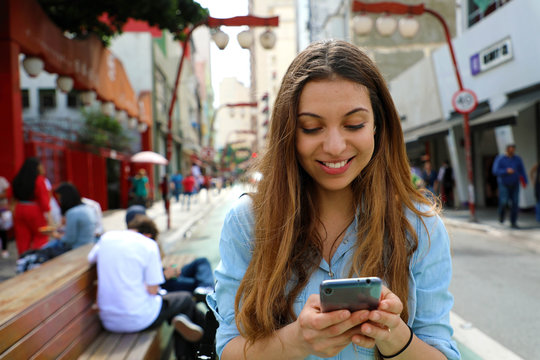 Portrait of a smiling young woman walking in the Sao Paulo City with cellphone, Brazil