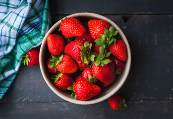Close-up of fresh strawberries in a bowl on wooden background, top view