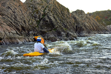 A man dressed as a monster big pasta (macaroni) in kayak paddling on rapid whitewater river at dusk. Funny costume sports show on the water