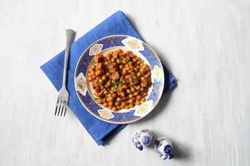 chickpea with meat made in red sauce served in white and blue plate with fork and  salt, pepper pot