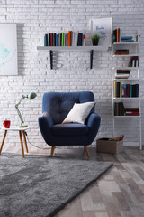 Room interior with comfortable armchair and different books near brick wall