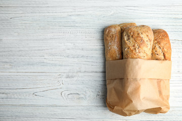Mini baguettes in paper bag on wooden table, top view with space for text. Wholegrain bread