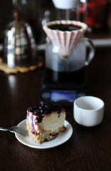 Piece of blueberry cheesecake on a white plate side view. Coffee in origami dripper. Delicious dessert