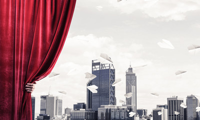 Modern business cityscape behind curtain opened by businessman hand