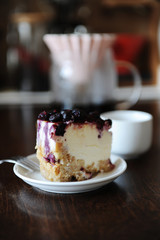 Piece of blueberry cheesecake on a white plate side view. Coffee in origami dripper. Delicious dessert