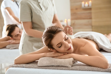 Fototapeta na wymiar Romantic young couple enjoying herbal bag massage in spa salon