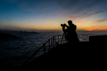 silueta de fotografo en puerto durante el anochecer usando tripode